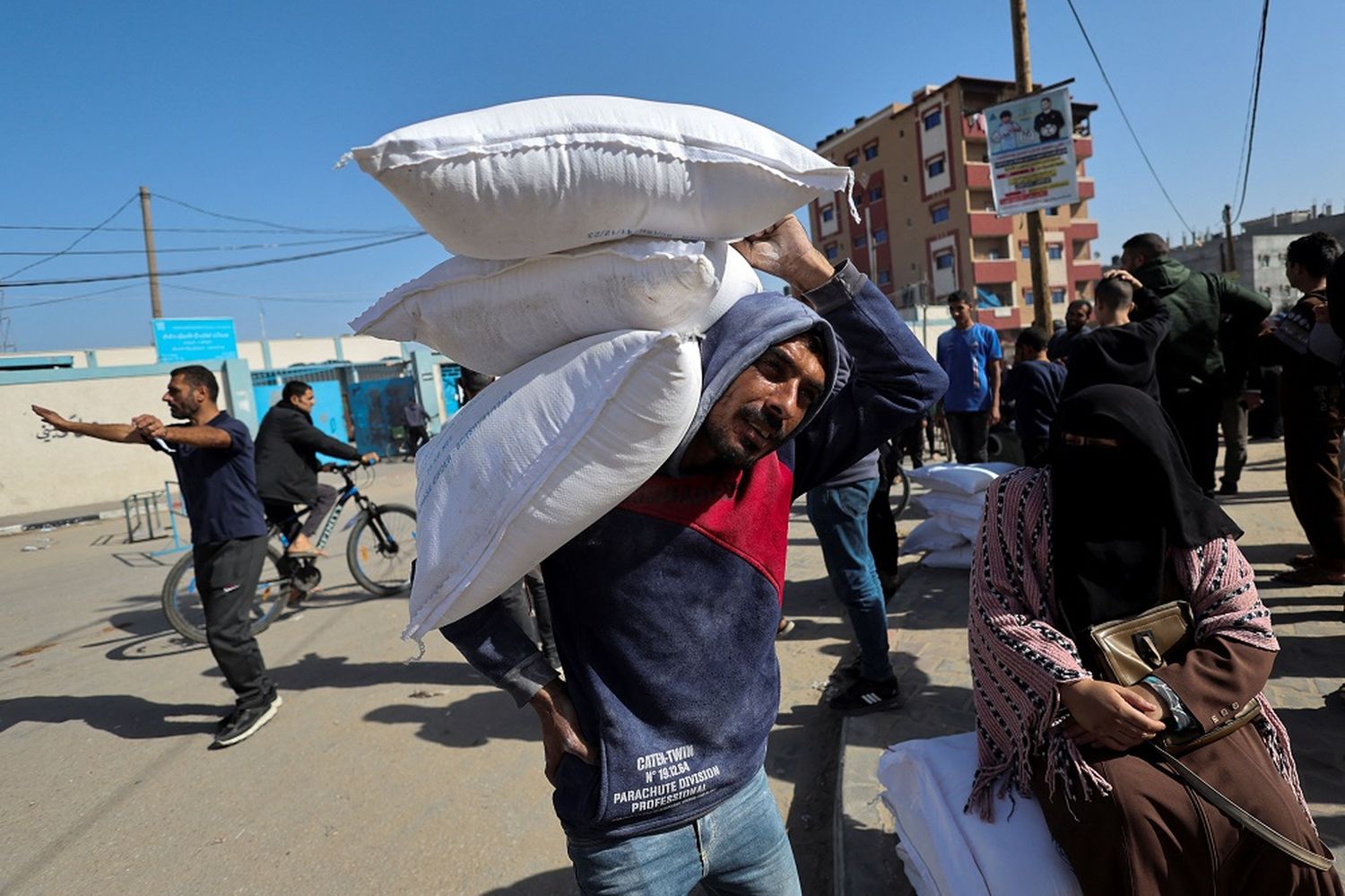 Un hombre lleva bolsas de harina mientras los palestinos se reúnen para recibir alimentos distribuidos por Naciones Unidas.