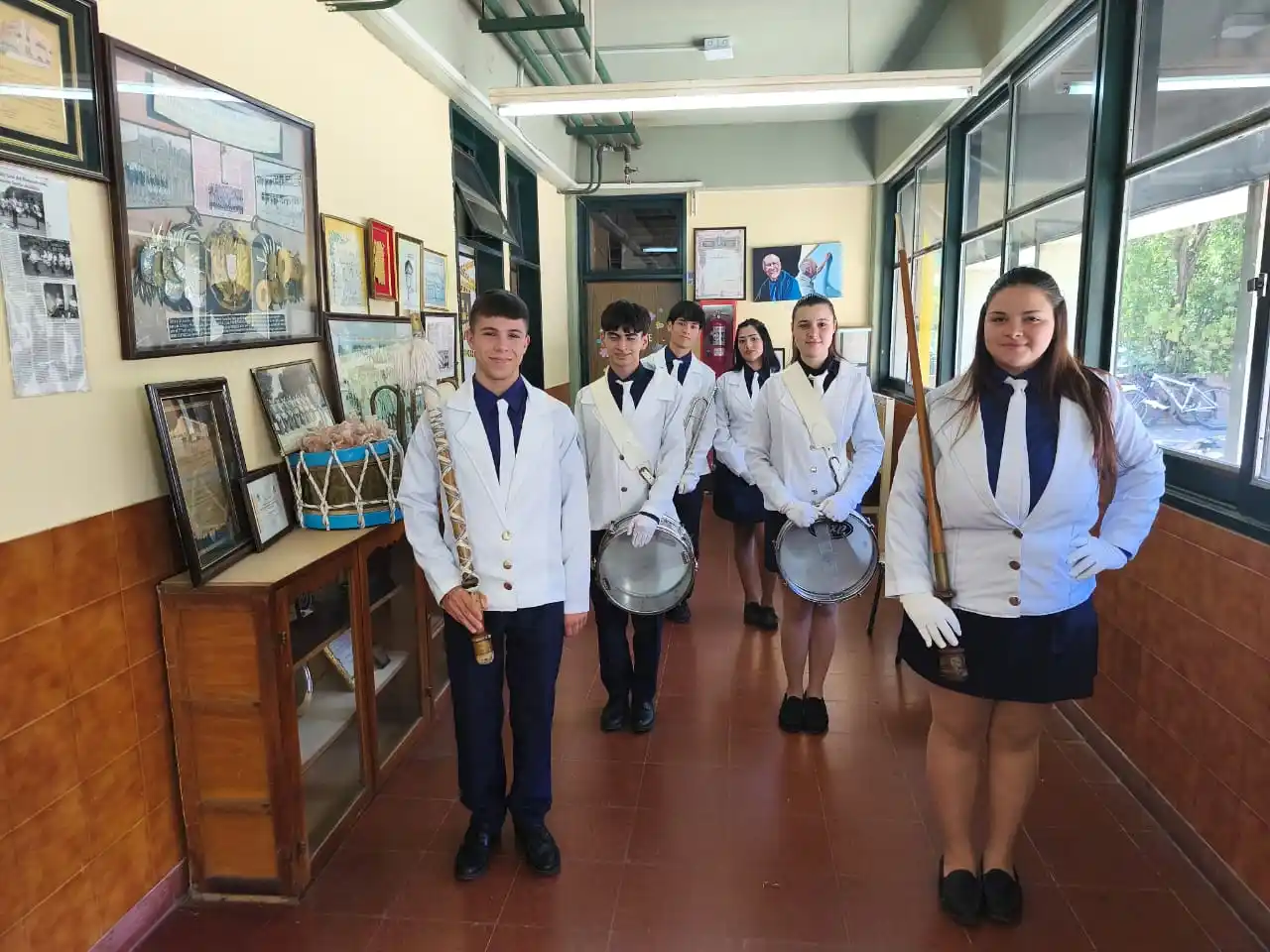 Las actuales autoridades de la Banda Lisa del San Martín posan en el histórico pasillo de la escuela y exhiben con orgullo el nuevo hallazgo patrimonial.