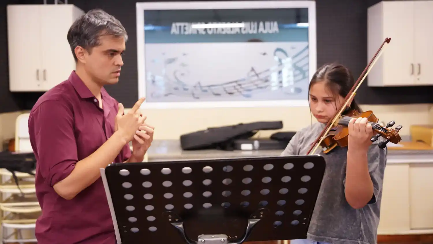 Jázmín y Pedro: Pedro guía con dedicación a Jazmín en una de sus clases de violín, afinando técnica, expresión y confianza