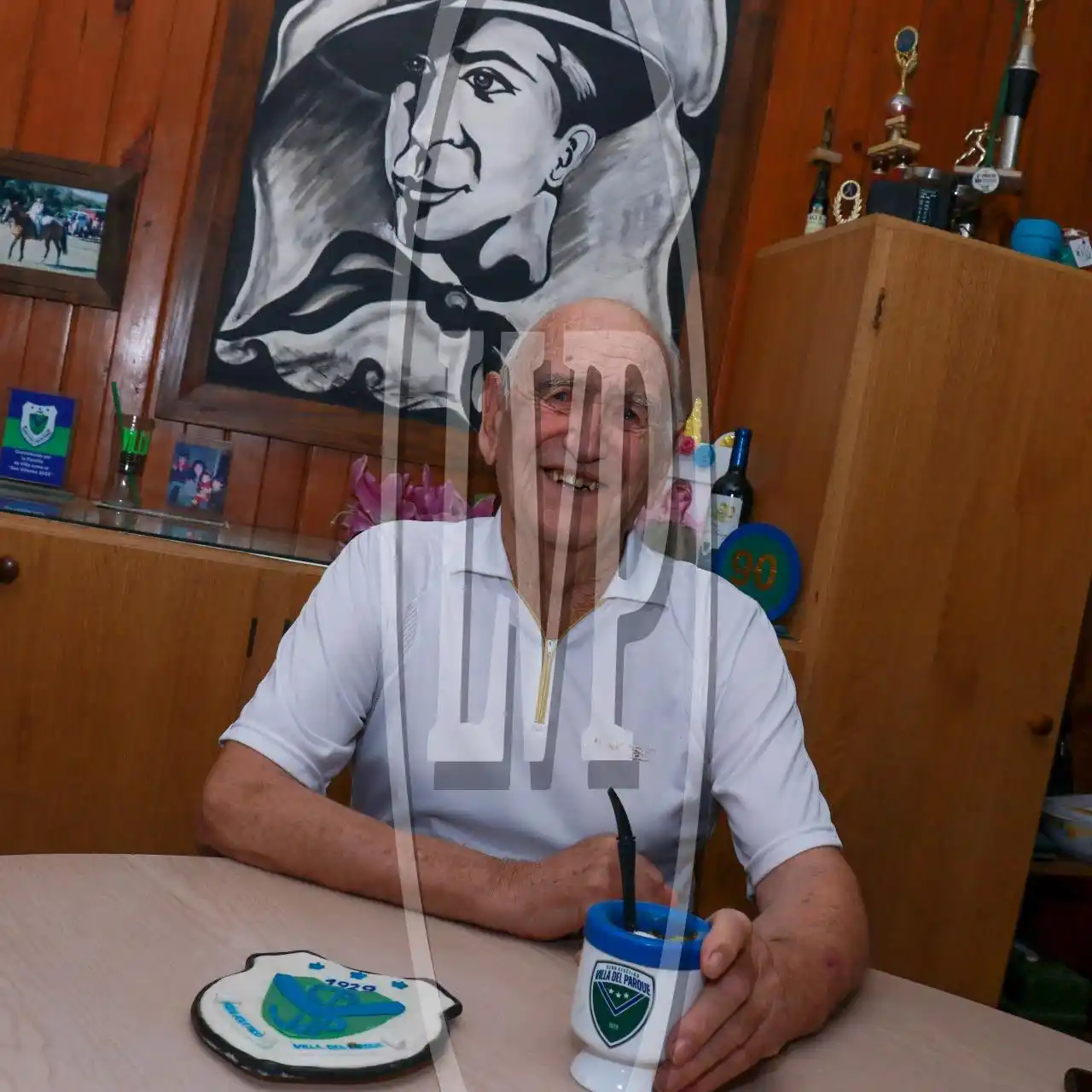 En el living de su casa. Pedro Rocha con el mate y un escudo de Villa. Detrás la pintura de Carlos Gardel, realizada por Mirta Rey