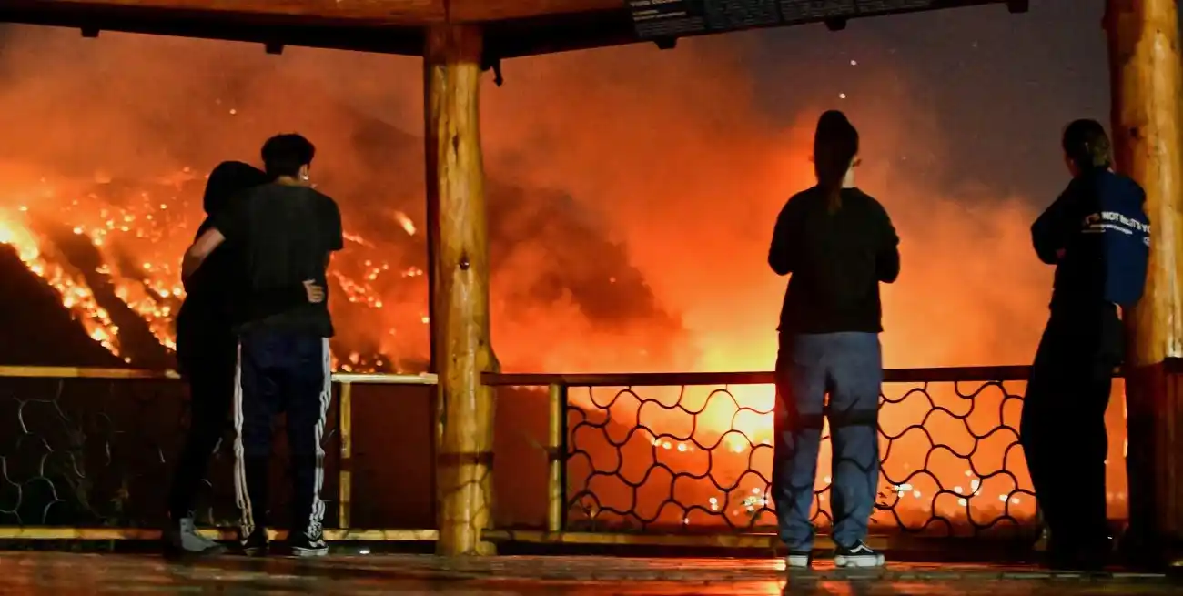 Personas observan el humo y las llamas que se elevan entre los árboles mientras se desarrolla un incendio forestal, en El Hoyo, en la provincia patagónica de Chubut, Argentina, el 7 de enero de 2026. REUTERS/Maxi Jonas
