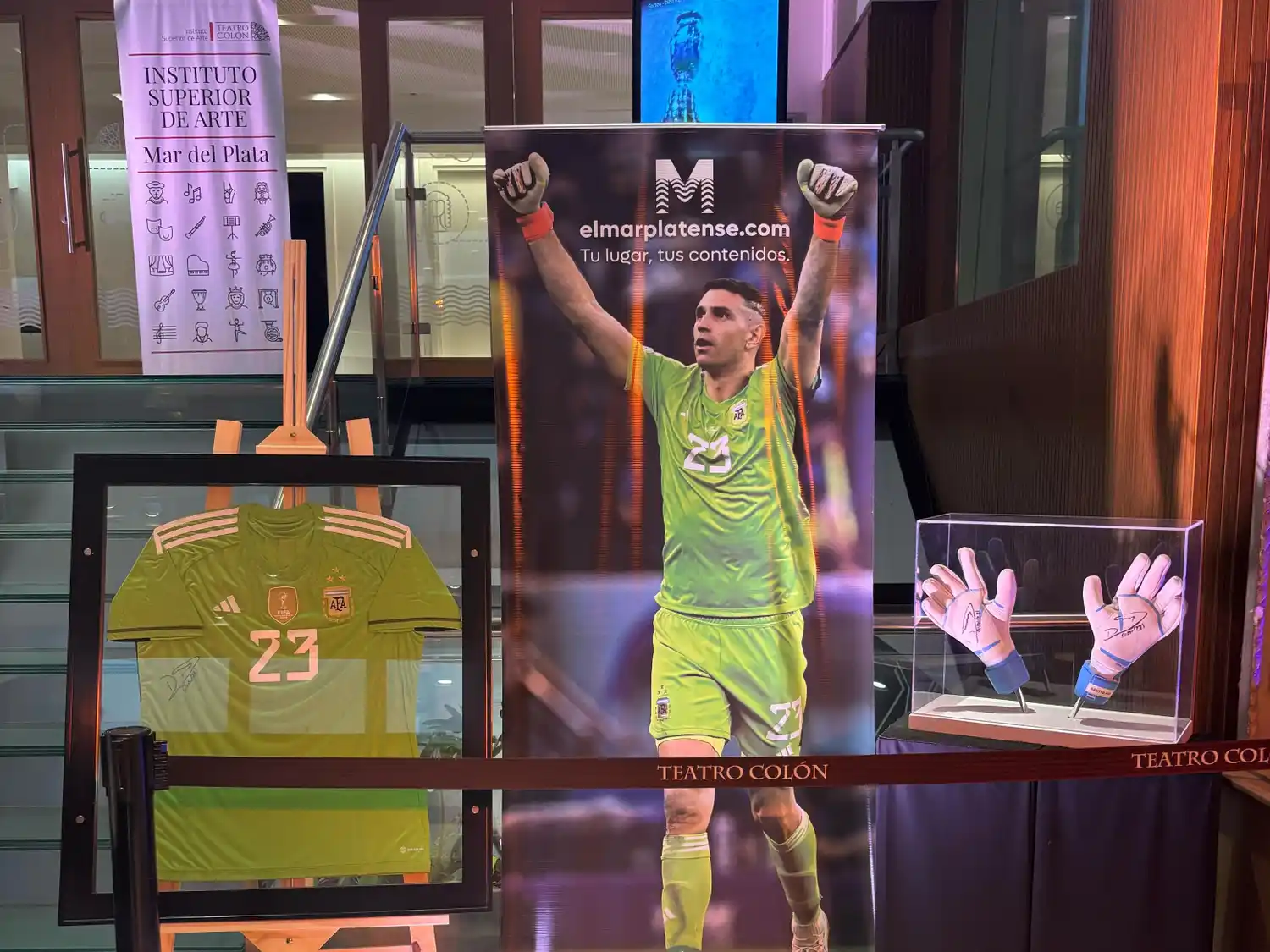 Quien se tome una foto con la camiseta o los guantes de Dibu en el Teatro Tronador, participa para viajar a ver el Superclásico Sudamericano.