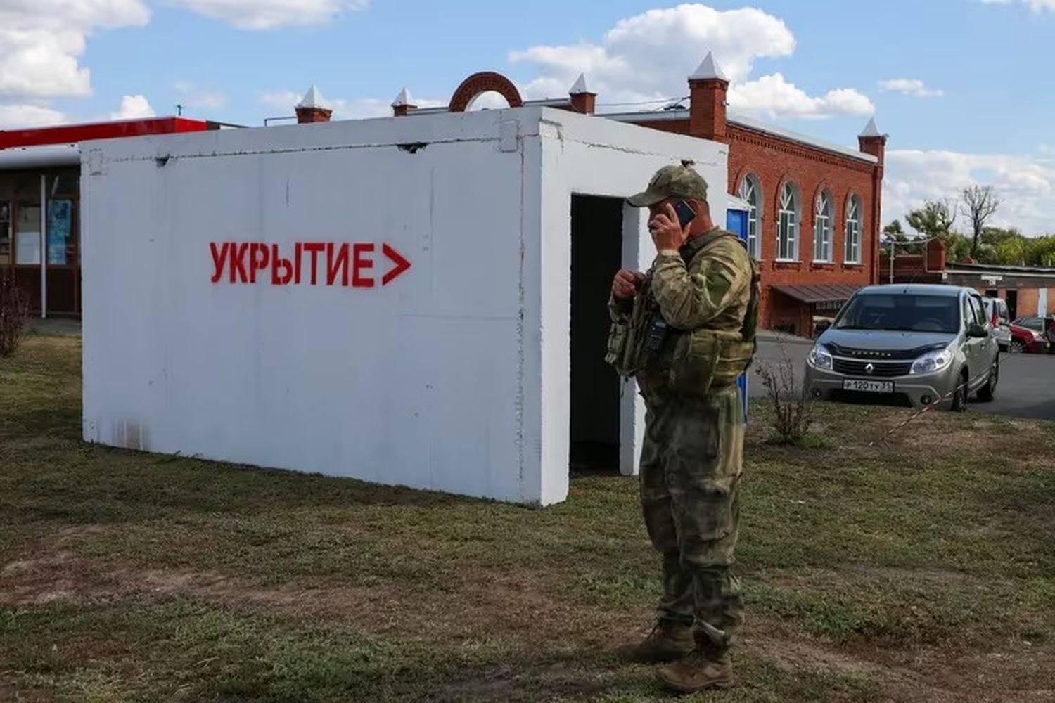 Un militar habla por teléfono junto a un refugio antiaéreo en un puesto de control en las afueras en Belgorod. Un cartel en la construcción reza: "Refugio (antibombas)".