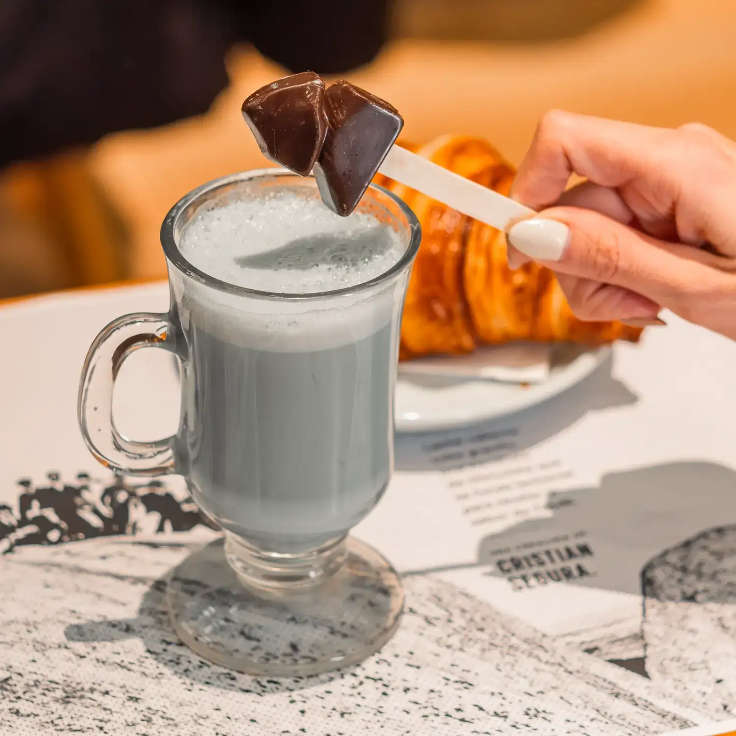 La obra invita a dejar caer una pequeña Piedra Movediza de chocolate en un vaso de leche gris, un gesto simple que convierte a cada persona en parte de la experiencia.