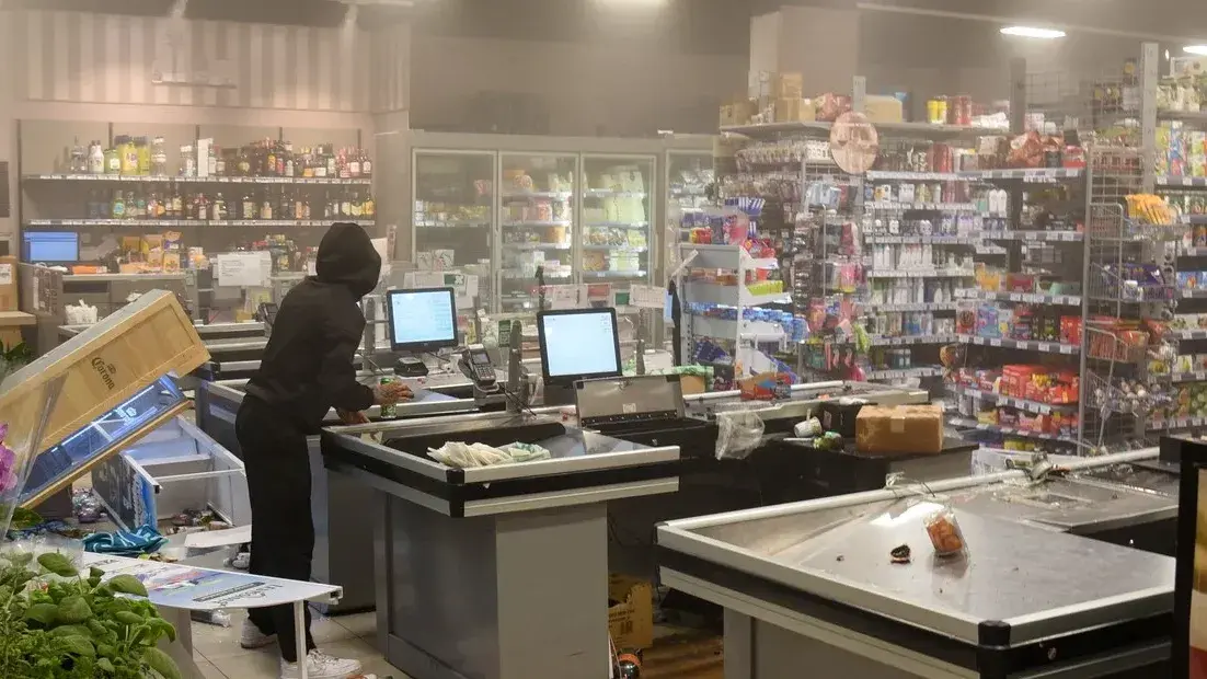 Un encapuchado permanece de pie cerca de una caja registradora dentro de un supermercado dañado durante las protetas en Milán.
