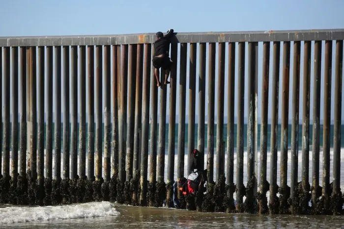 Un migrante sube la valla fronteriza para cruzar a Estados Unidos y solicitar asilo en Playas de Tijuana. Crédito: Jorge Duenes / Reuters
