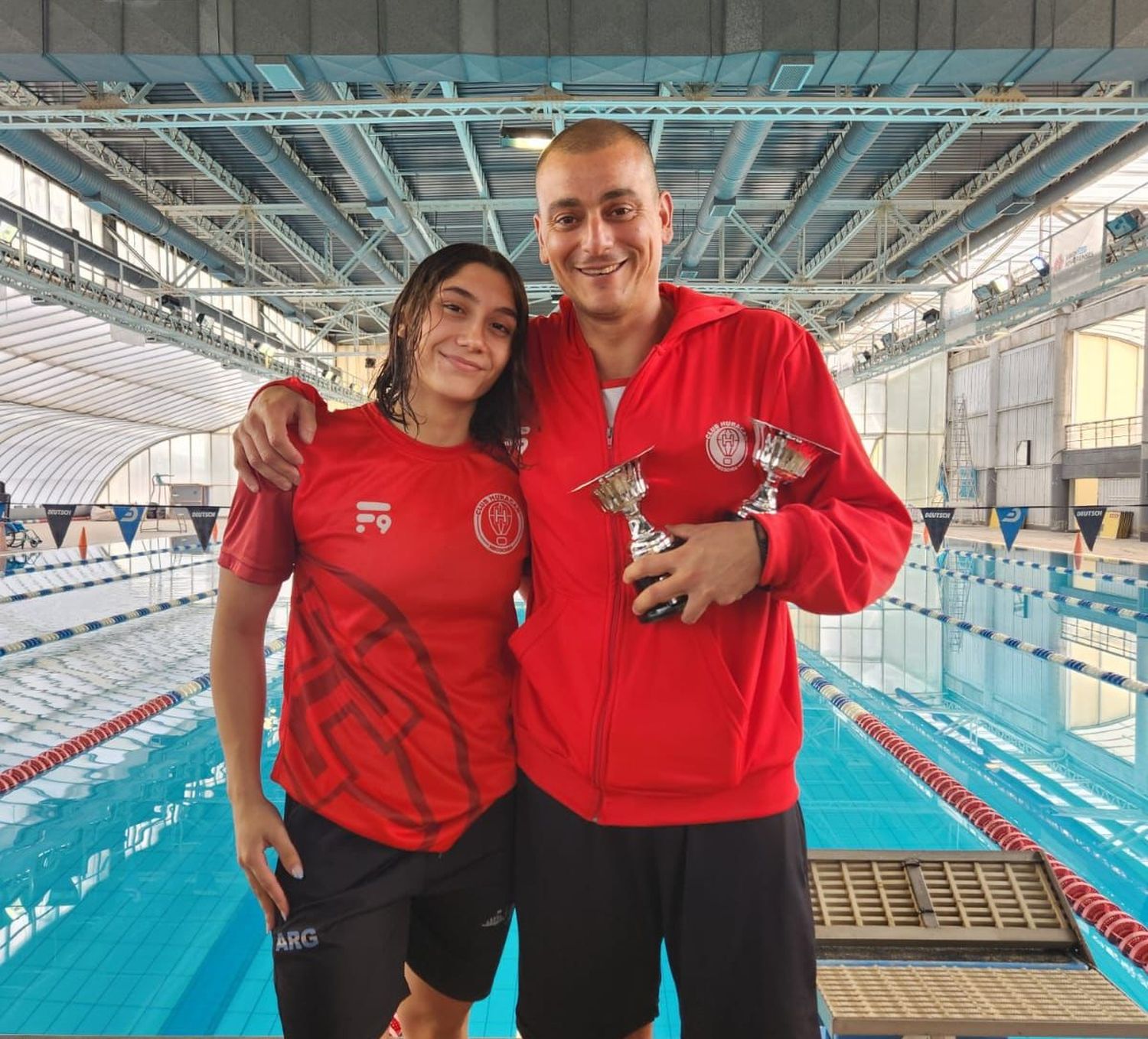 Guadalupe Angiolini con su entrenador Claudio Castagnari y los trofeos que ganó por sus marcas técnicas