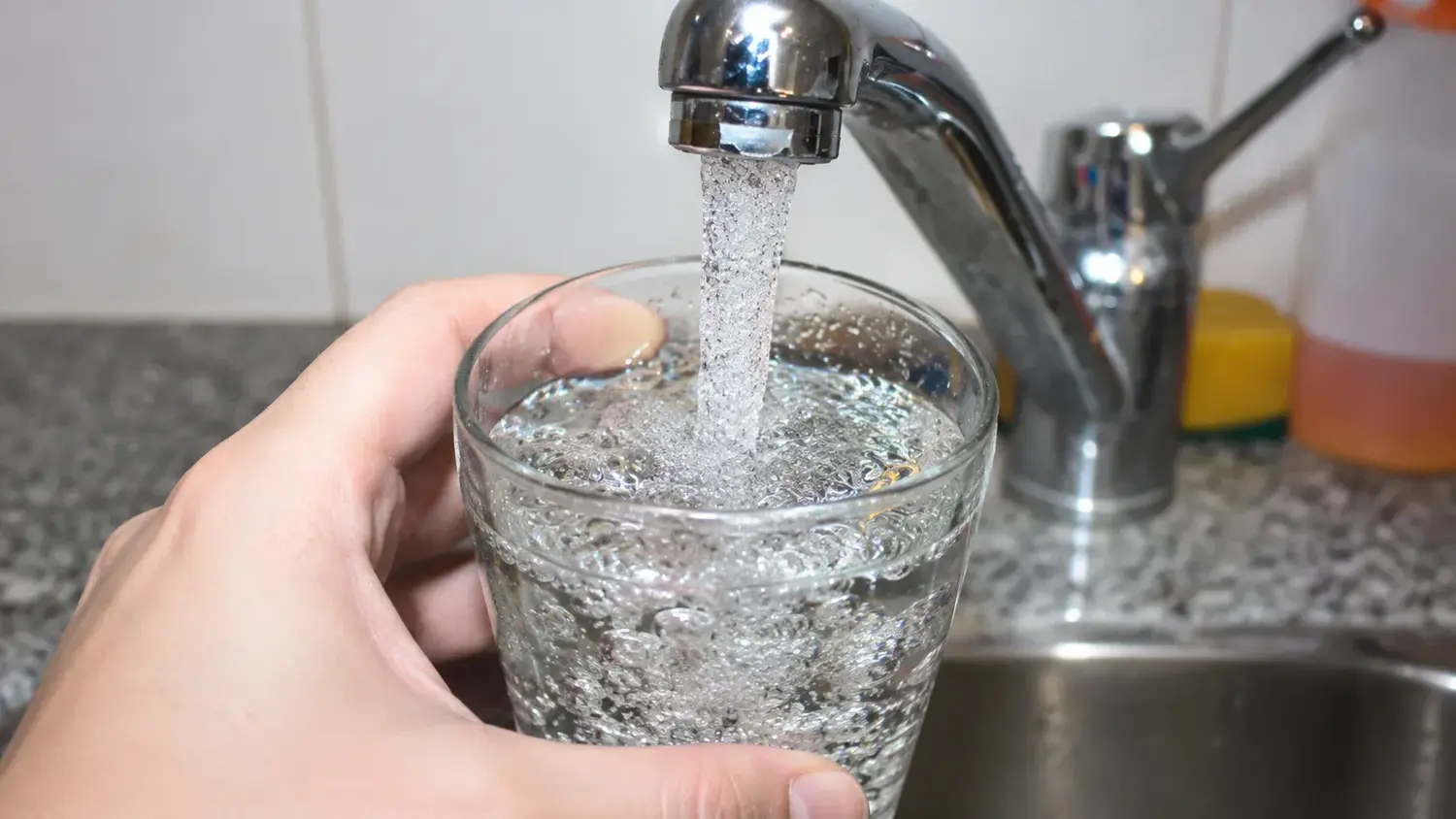 Una mano sostiene un vaso de vidrio mientras se llena con agua.