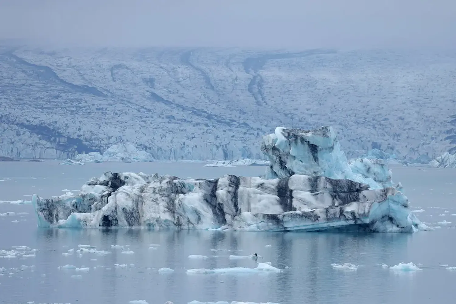 An iceberg broken from the glacier Breidamerkurjokull, which looms behind.