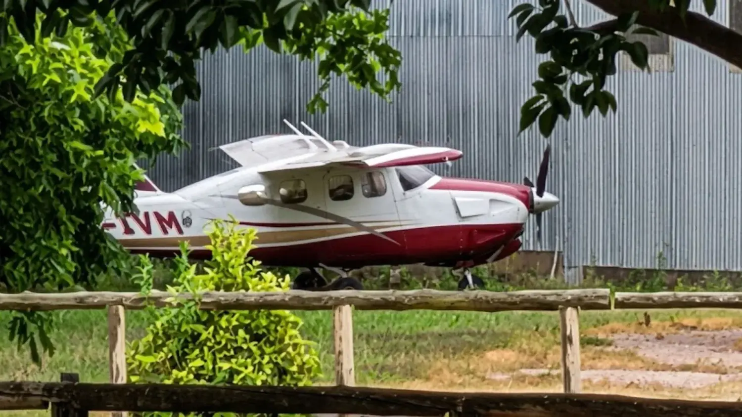 El narcoavión permanece abandonado en el Aeroclub San Pedro tras cinco años de secuestro judicial. La aeronave blanca y roja se encuentra estacionada frente a un galpón, rodeada de vegetación y cercos de madera a la espera de una resolución.