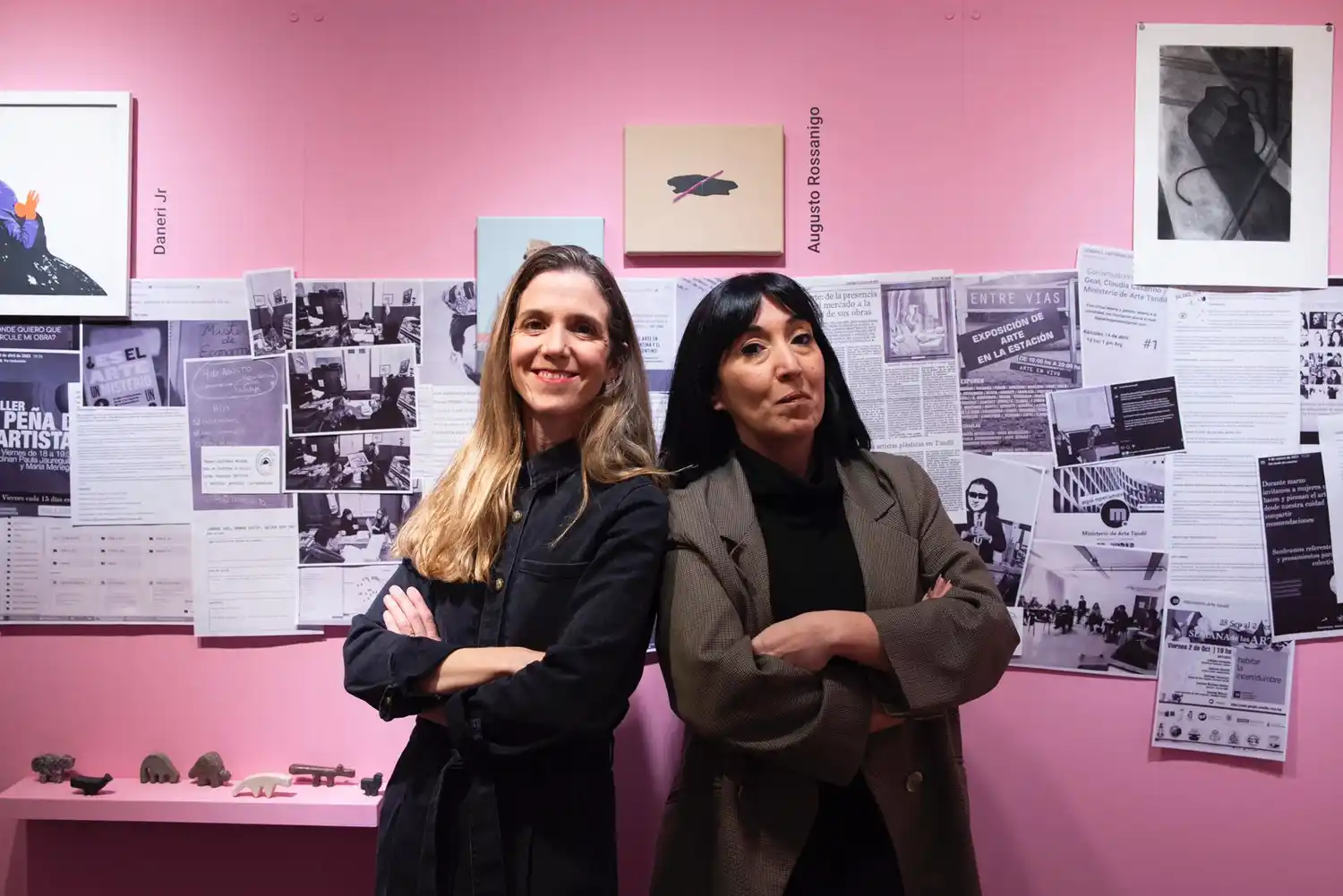 María Menegazzo y Paula Jaureguiberry, del Ministerio de Arte Tandil, con parte de la muestra Reporte Ministerial de fondo.