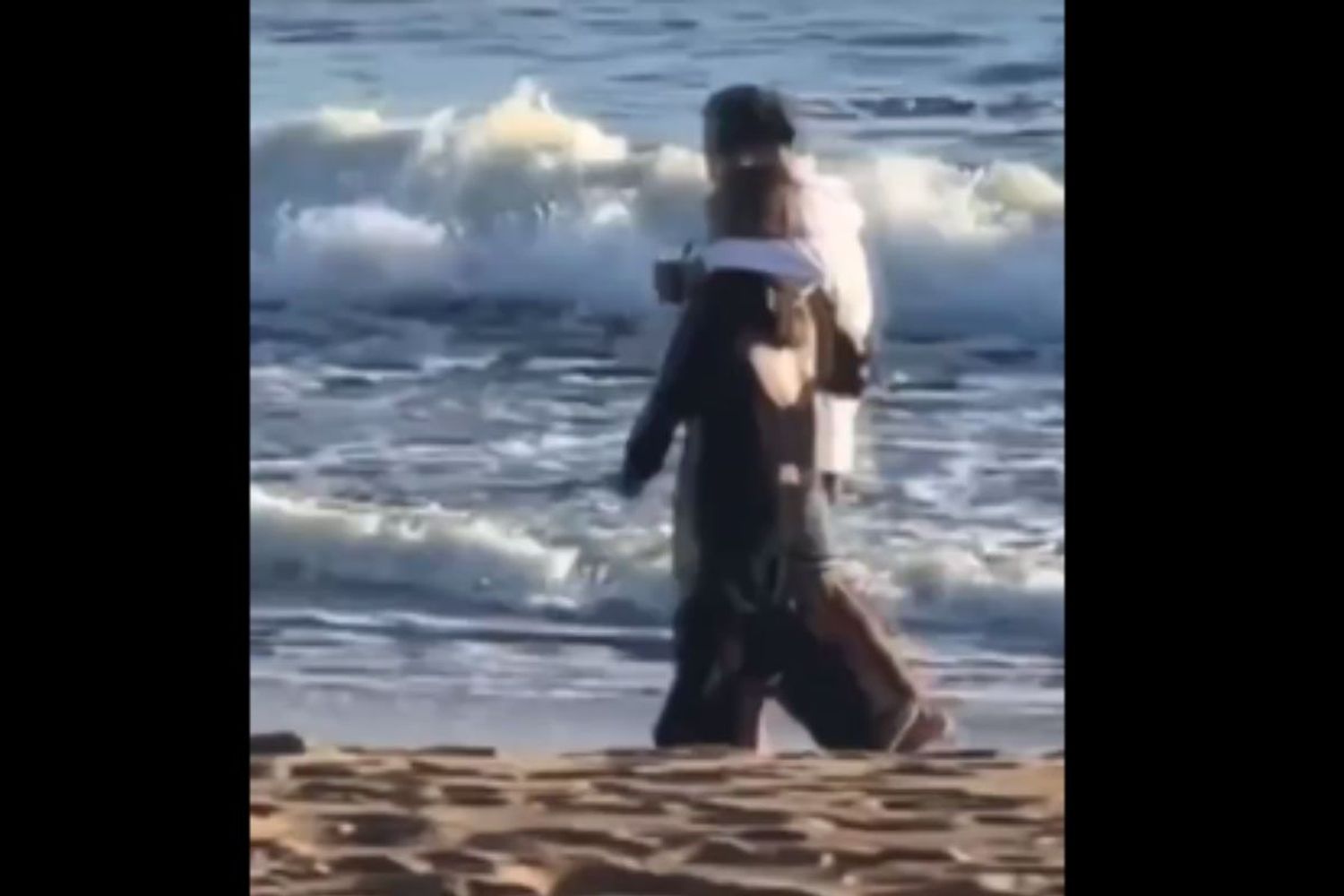 En compañía de un hombre misterioso, caminando abrazados junto al mar.