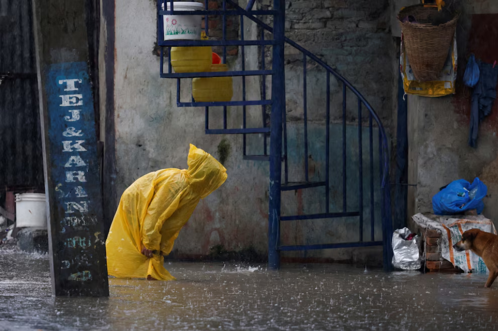 Una mujer con chubasquero vadea una calle inundada junto a la orilla del desbordado río Bagmati tras las fuertes lluvias, en Katmandú, Nepal. 4 de octubre de 2025. REUTERS/Navesh Chitrakar