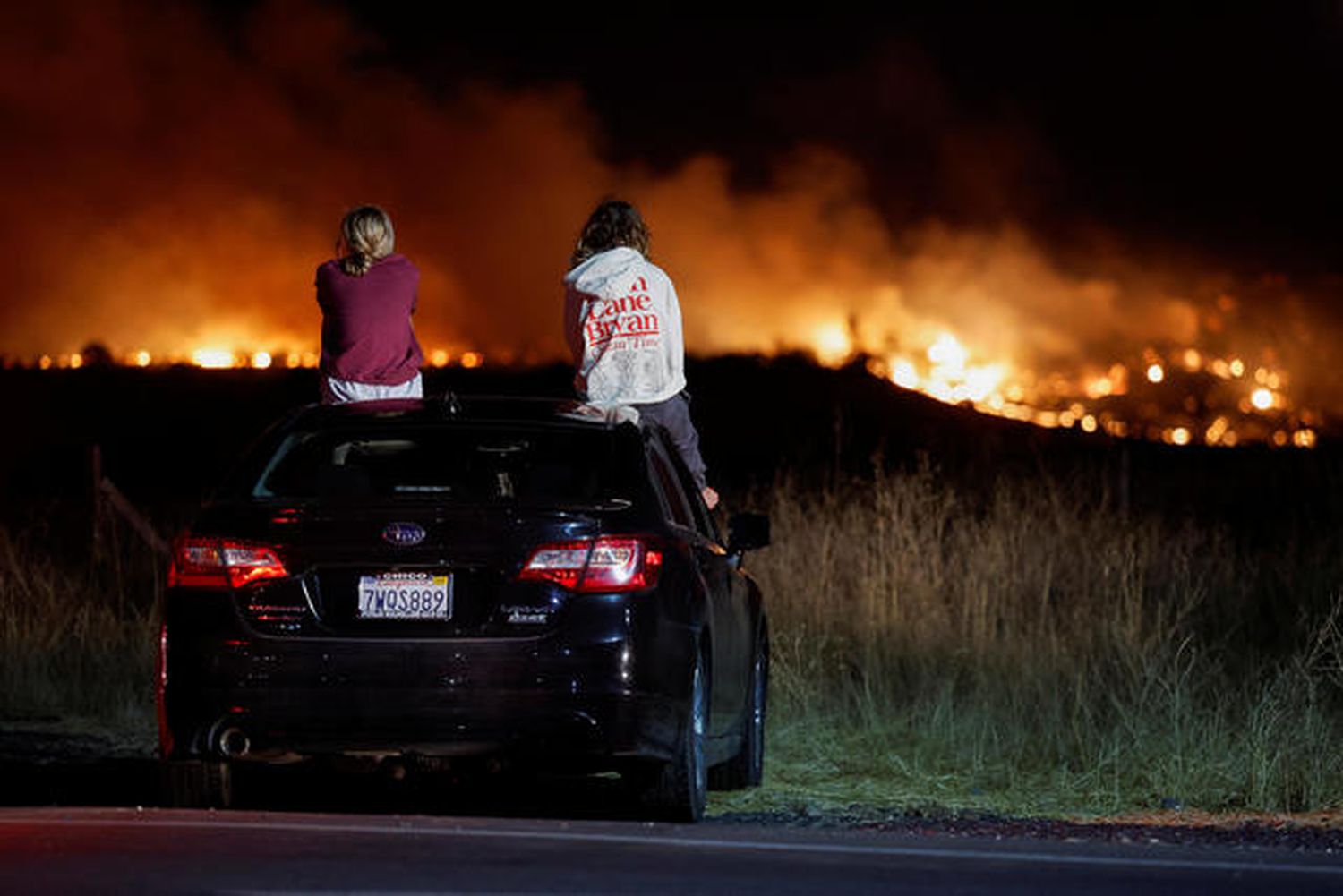 Lily Moore and Megan Panighetti watch the Park Fire burning as they sit on top of a car in Chico, California, on July 25, 2024.