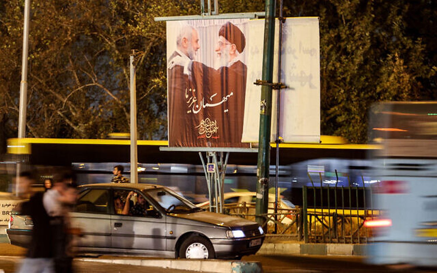 Vehicles move past a banner depicting Iran's Supreme Leader Ayatollah Ali Khamenei embracing Ismail Haniyeh, the slain leader of Hamas, in Tehran's Azadi Square on August 13, 2024.