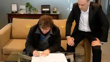 Milei firmando, en compañía de Adorni.