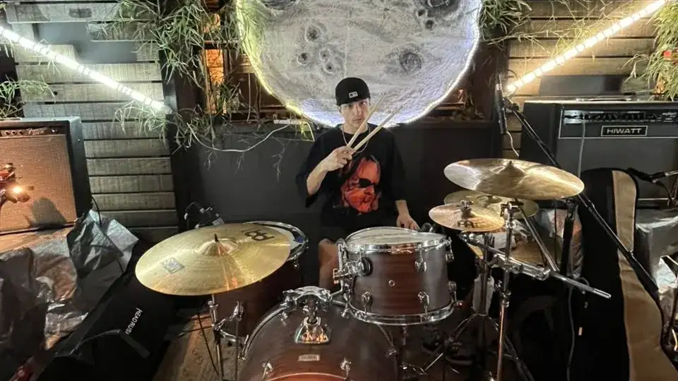 El baterista Franco Molina posa frente a su batería profesional en un estudio ambientado con luces led y una decoración lunar, reflejando la dedicación y el talento que definen su carrera musical en la escena artística de Tandil.