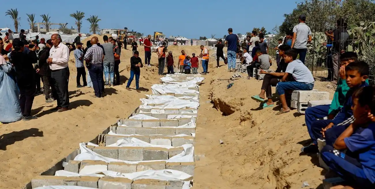 Los dolientes se reúnen junto a un lugar de entierro masivo de cuerpos no identificados de palestinos que habían estado retenidos en Israel durante la guerra, después de que fueron entregados por Israel, en medio de un alto el fuego entre Israel y Hamás en Gaza, en Deir Al-Balah, en el centro de la Franja de Gaza. Crédito: REUTERS/Mahmoud Issa