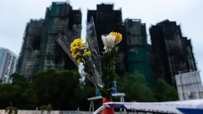 La gente ofrece flores a las víctimas cerca del lugar del incendio del miércoles en Wang Fuk Court, una urbanización del distrito de Tai Po, Hong Kong, el 30 de noviembre de 2025. [Chan Long Hei/AP]