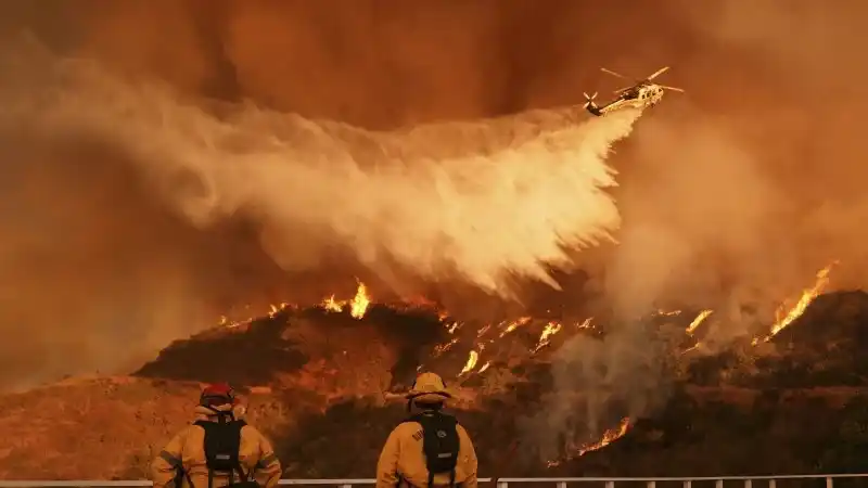 Bomberos observan cómo un helicóptero lanza agua sobre el incendio Palisades en el cañón Mandeville, Los Ángeles, el 11 de enero de 2025. (Foto AP/Jae C. Hong, Archivo)