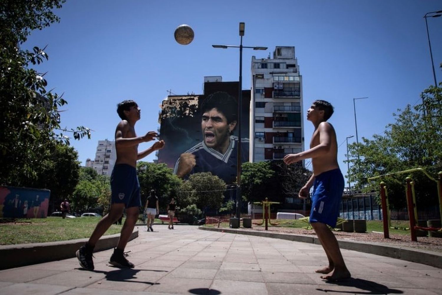 Jóvenes jugando al fútbol frente al mural de Martín Ron en homenaje a Diego Armando Maradona. Crédito: Xinhua/Martín Zabala