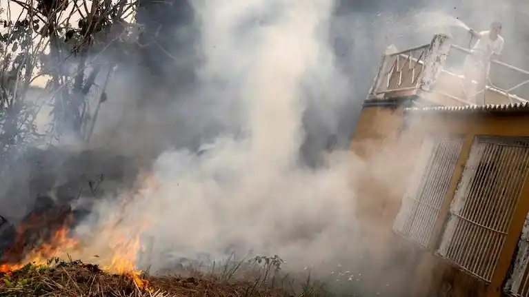 Una mujer intentan apagar con una manguera un incendio junto a su casa a orillas del río Madeira en Porto Velho, en Brasil
