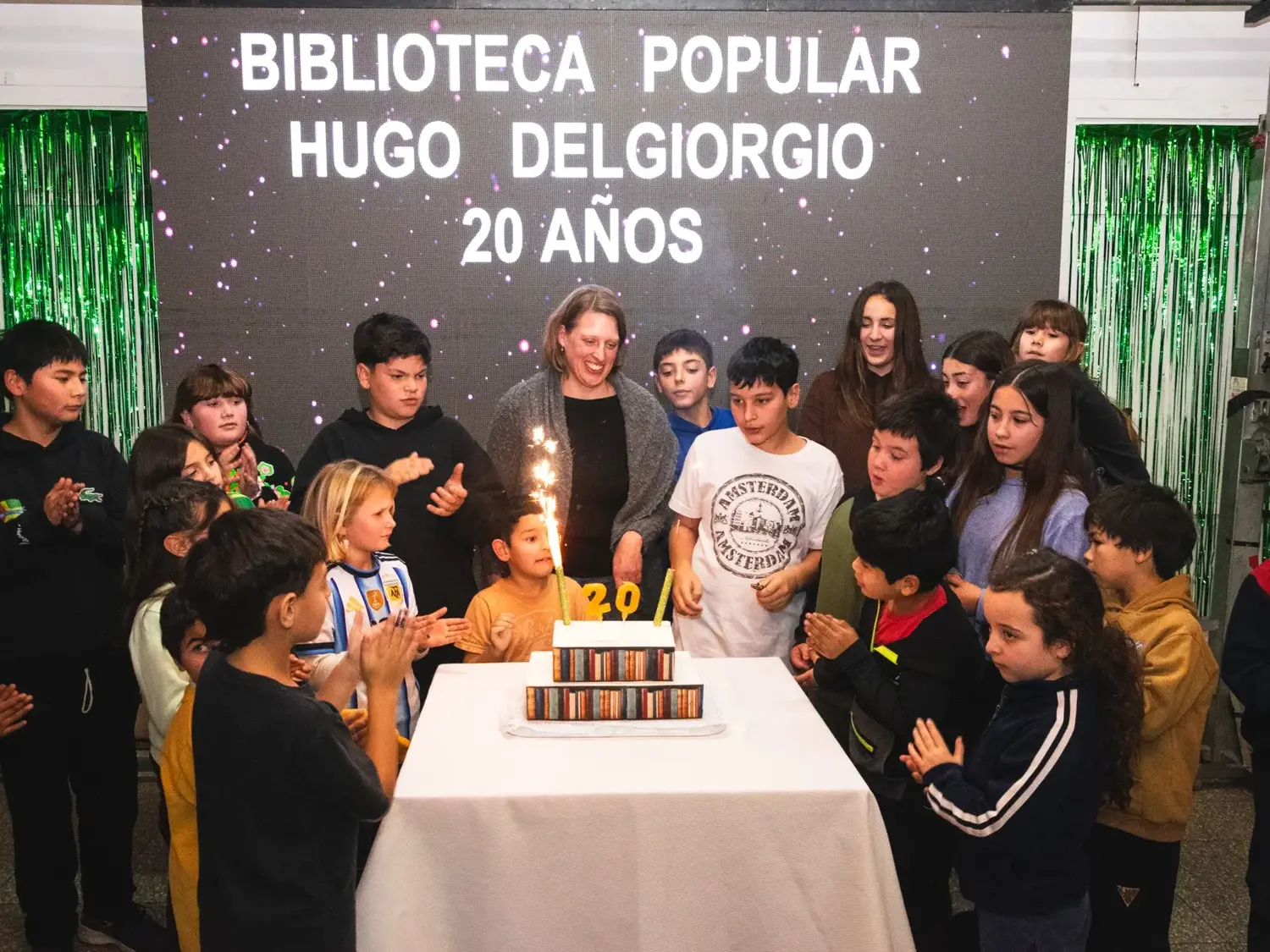 “¡Que los cumplas feliz…!”. La bibliotecaria Sofía Kisbye y los chicos, con la torta del 20º aniversario