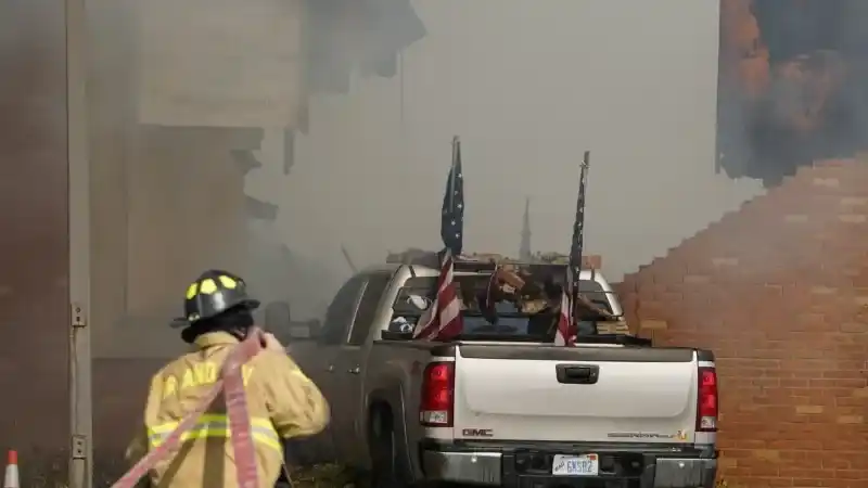 Un vehículo que fue embestido contra el edificio está rodeado de humo mientras un bombero trabaja en el lugar en la Iglesia de Jesucristo de los Santos de los Últimos Días en Grand Blanc, Michigan, el domingo 28 de septiembre de 2025. (Lukas Katilius/The Flint Journal vía AP)