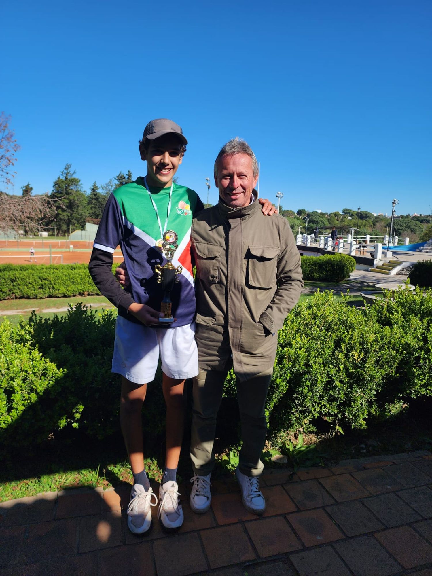 Luciano Cabaña exhibe el trofeo de campeón junto a su entrenador Ariel Zevallos.