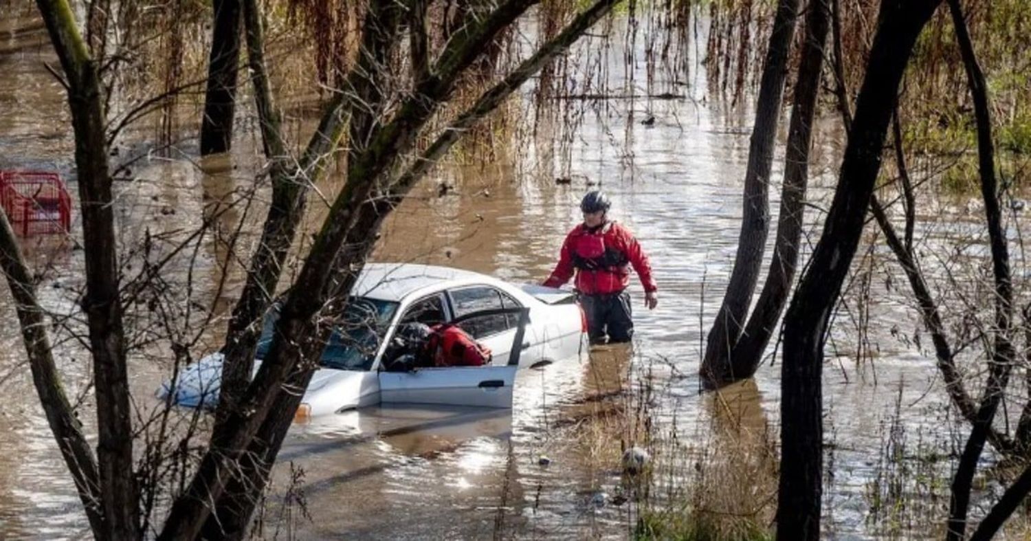 Trabajadores de búsqueda y rescate inspeccionan un automóvil alcanzado por una inundación generada por el aumento del caudal del río Guadalupe, en San José, California.