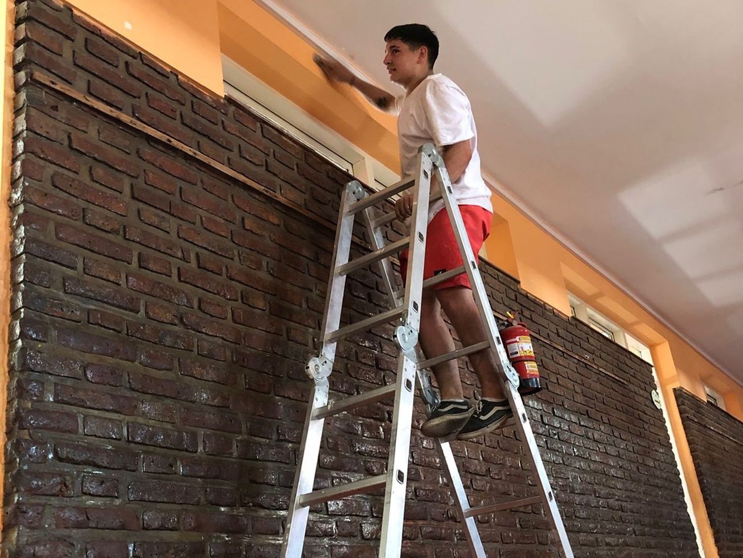 En la Escuela N° 969, lijando paredes en las alturas, en el proceso previo a la pintura.