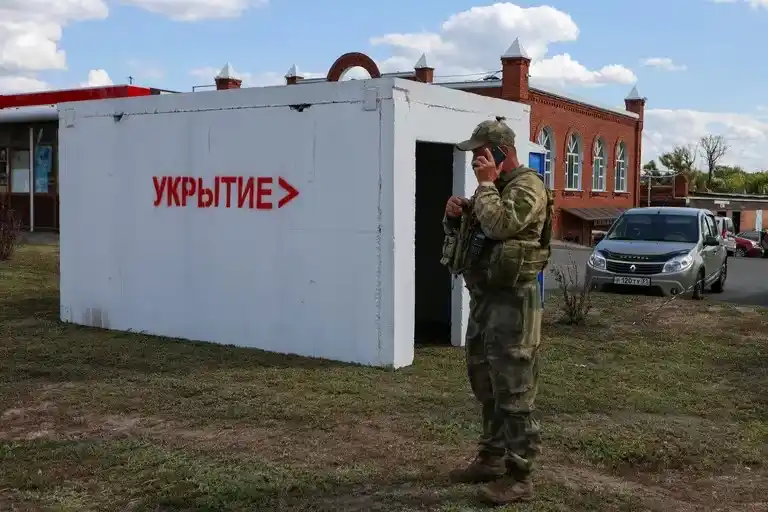 Un militar habla por teléfono junto a un refugio antiaéreo en un puesto de control en las afueras en Belgorod. Un cartel en la construcción reza: "Refugio (antibombas)".