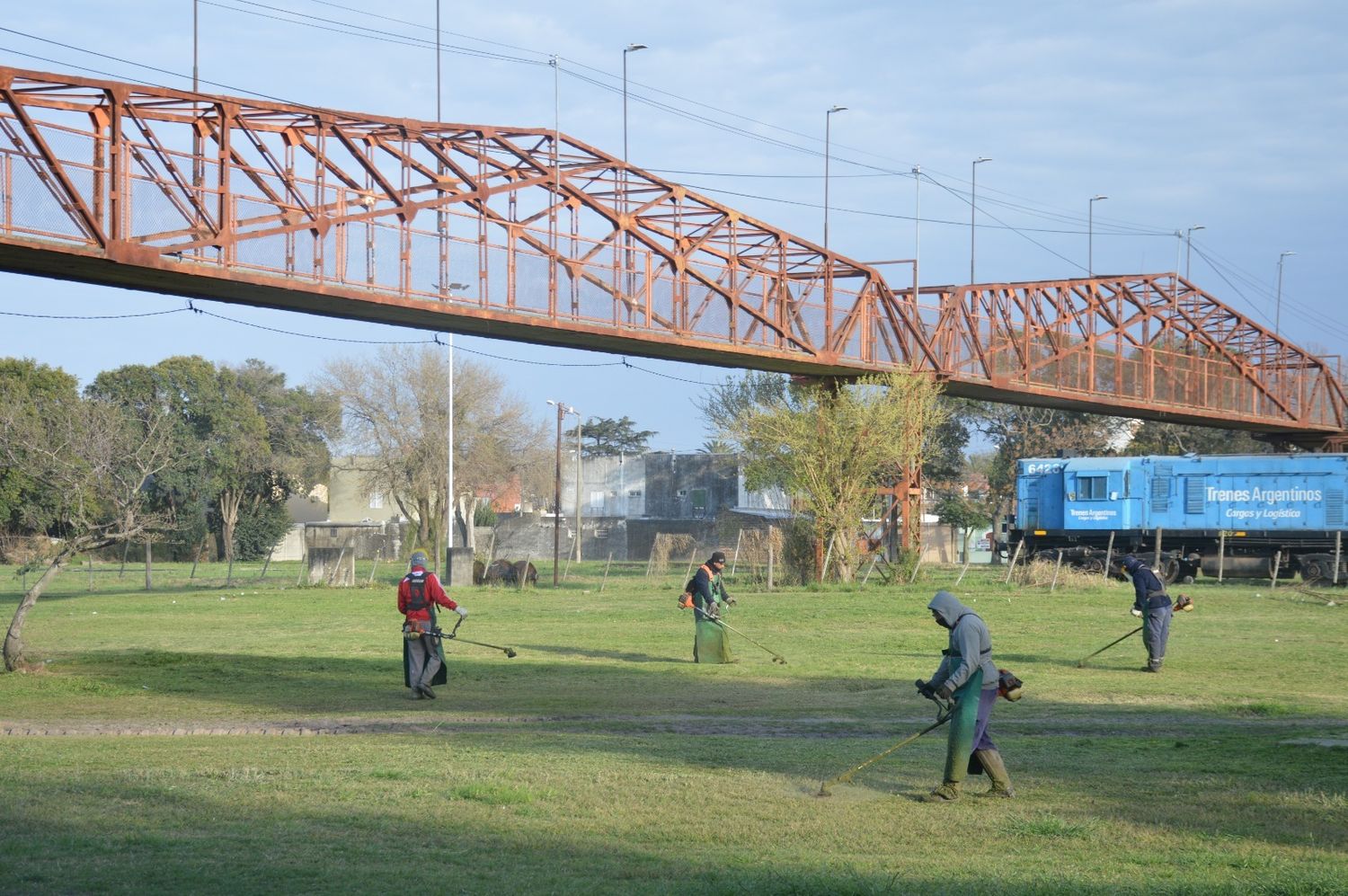 En la zona del ferrocarril, bajo el puente peatonal, los trabajadores proceden al corte de césped.