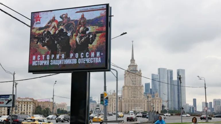 La gente camina junto a una pancarta de apoyo al ejército ruso en Moscú el 11 de agosto de 2025. La pancarta dice: «La historia de Rusia es la historia de los defensores de la patria». [Yulia Morozova/Reuters]