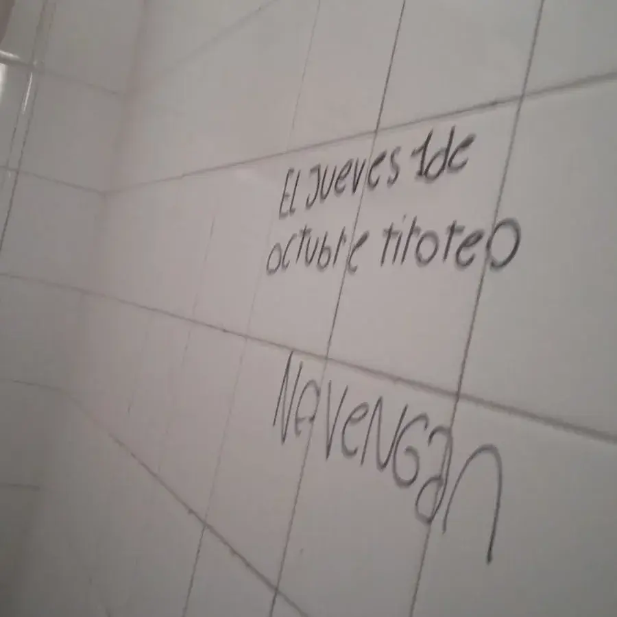 La imagen muestra la pintada realizada con fibrón negro sobre los azulejos blancos de un baño en la escuela Normal, donde se lee una amenaza de tiroteo que generó preocupación y alarma en toda la comunidad educativa de la institución.