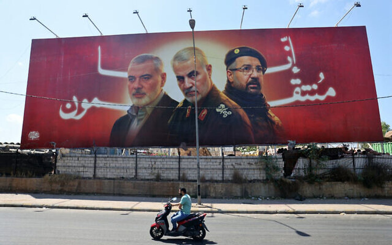 A man rides his moped past a billboard bearing portraits of slain terror leaders, Ismail Haniyeh of Hamas (left), Iranian Quds Force chief Qasem Soleimani (C), and Hezbollah senior commander Fuad Shukr on the main road near the Beirut International Airport on August 3, 2024.