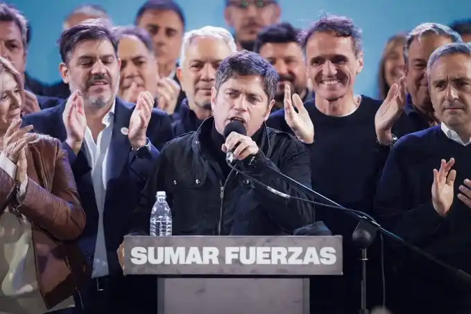 Axel Kicillof da un discurso tras el triunfo electoral, rodeado de su equipo en el escenario con el cartel "Sumar fuerzas".