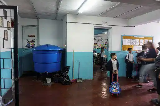 Los alumnos se paran cerca de un tanque de captación de agua de lluvia utilizado para abastecer de agua a los baños del preescolar Fermín Toro, beneficiario del programa "Lata de Agua", en el populoso barrio de Petare en Caracas